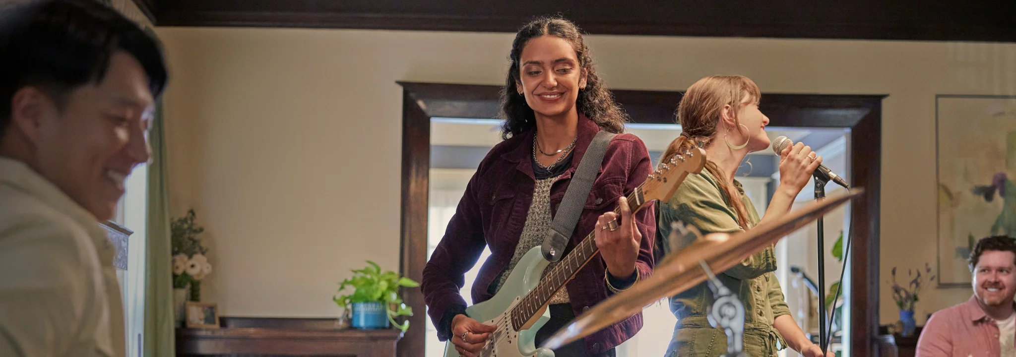 Woman smiling, playing bass guitar while another woman sings into microphone